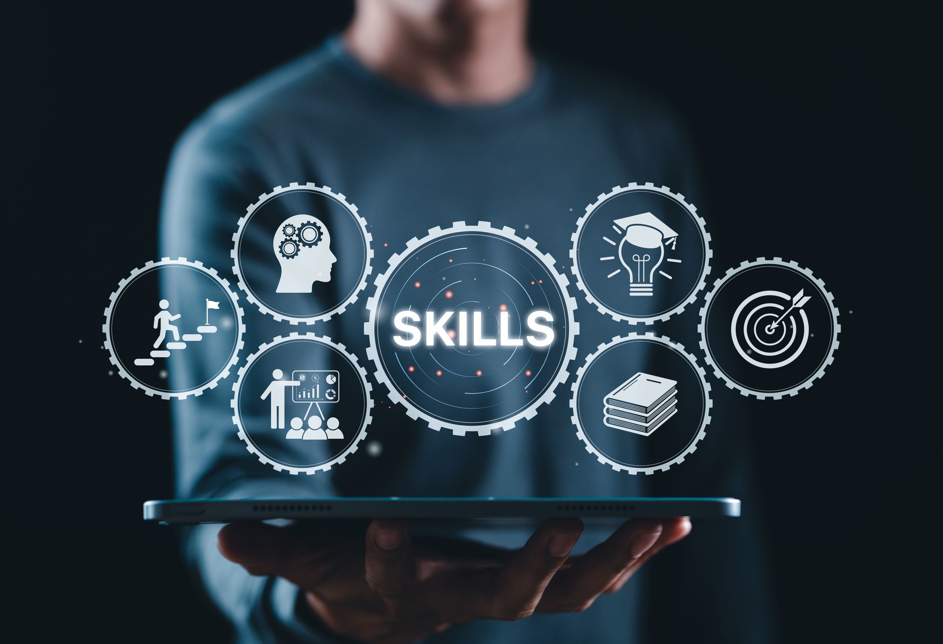 Skills Development and Professional Training Concept. Businessman holds tablet displaying gear icons with word "SKILLS," representing knowledge, growth, training, education, and personal development.