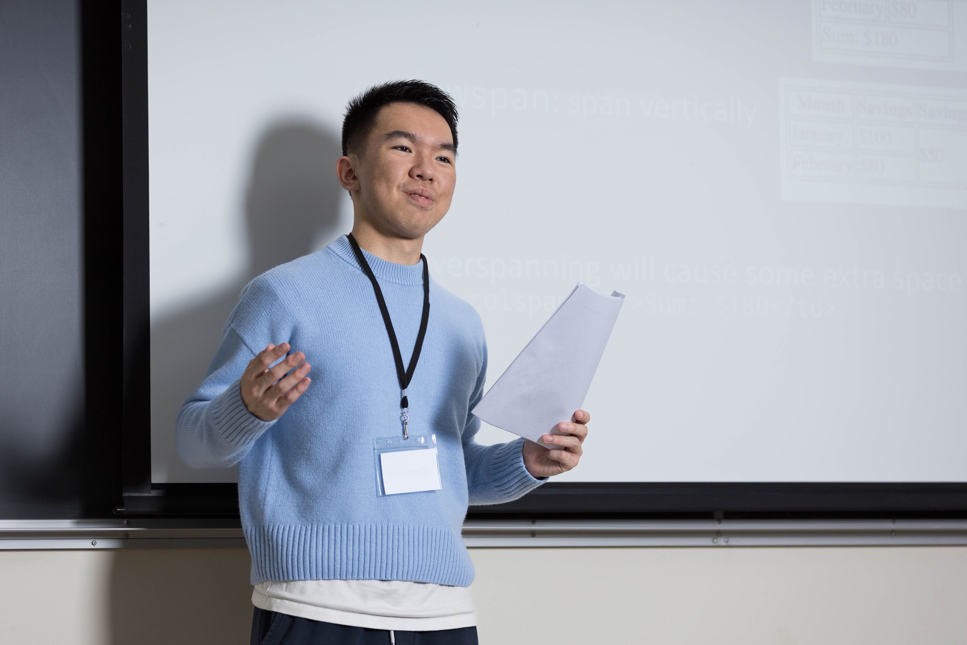 A man in a blue sweater is presenting in front of a whiteboard