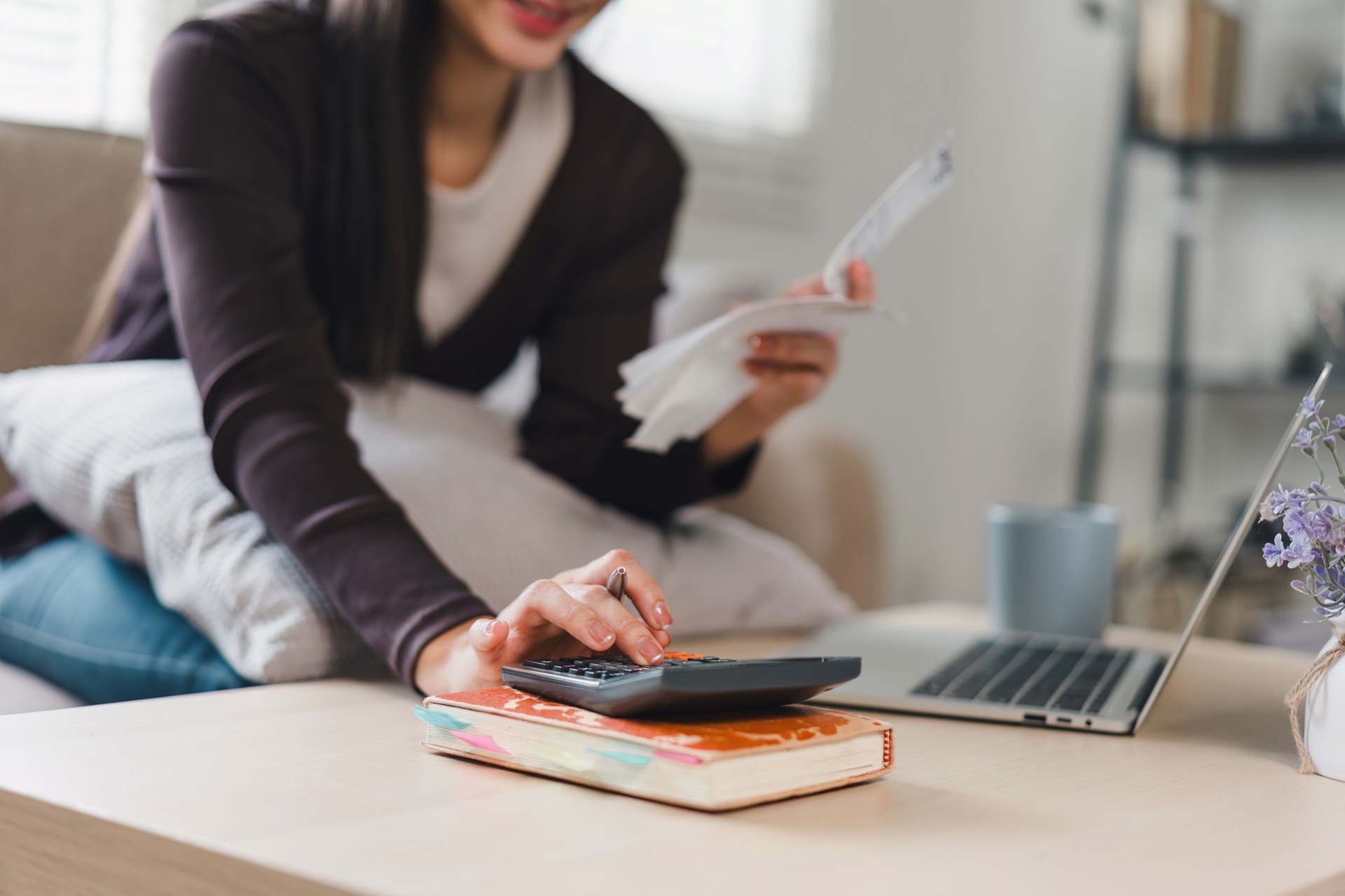 Close up of woman using calculator and holding receipts while managing finances at home.
